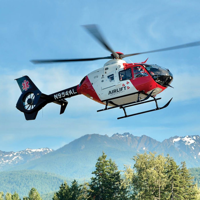 Airlift Northwest helicopter in flight in front of mountains and trees